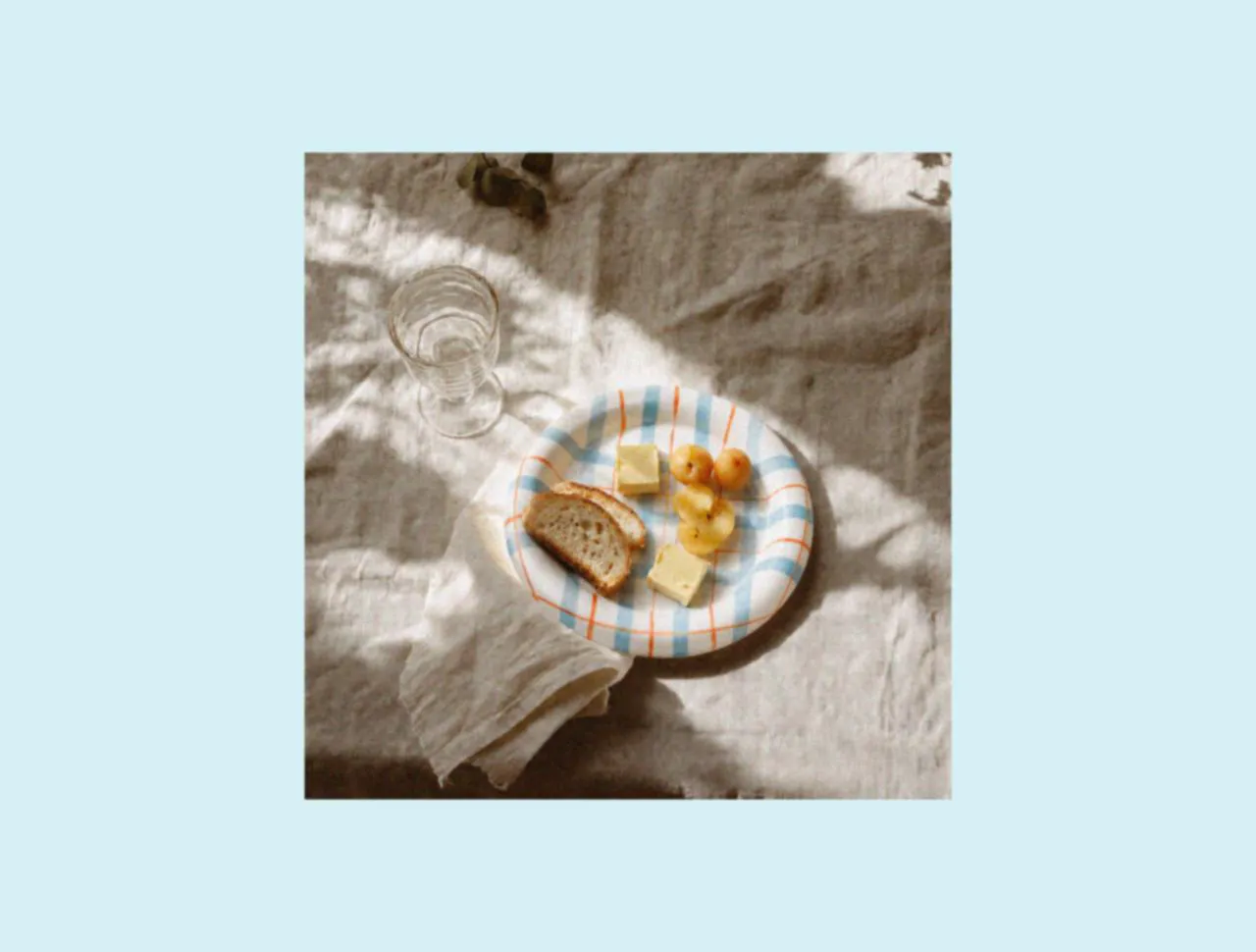 Ceramic dinner plates with bread and fruit on soft linen, styled as designer tableware and part of a picnic dinnerware set that brings the warmth of a relaxed family picnic into a first apartment.