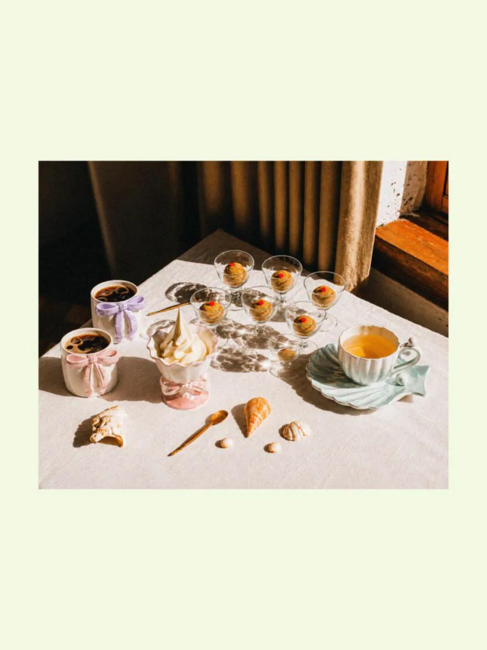 Table styled with a designer coffee mug, mugs for latte, and ice cream cups, surrounded by summery things and beach shell details, with a soft mugs gift set atmosphere in warm summer light.